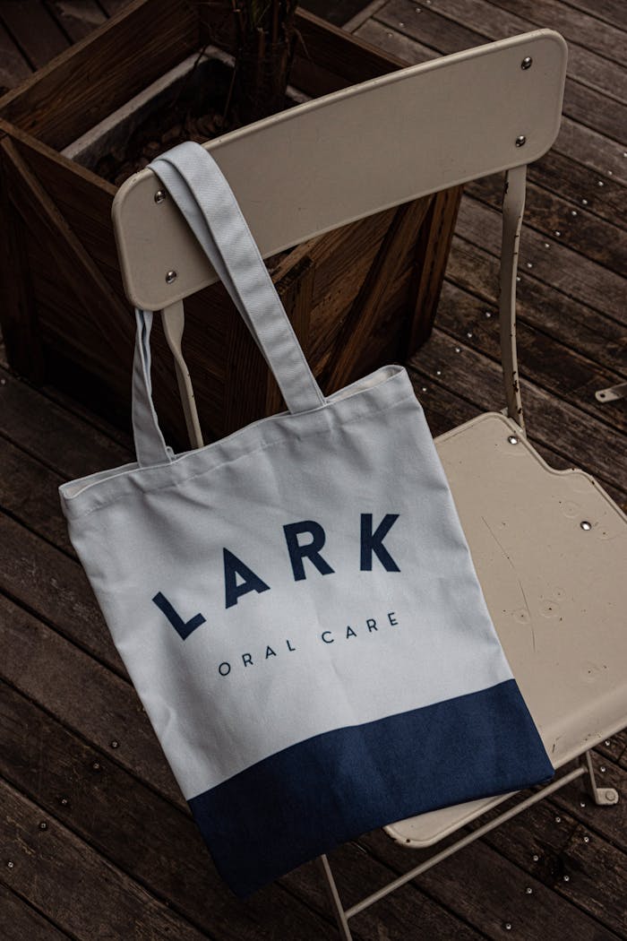 A modern tote bag with 'Lark Oral Care' branding hangs on a white chair in an outdoor setting.